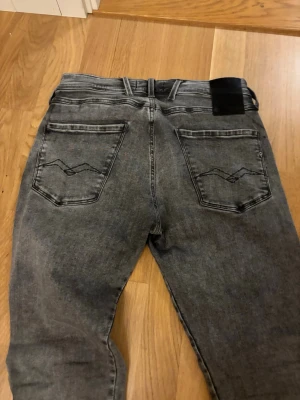 Replay Anbass grå jeans slim- fit - Säljer ett par Replay Anbass jeans, väldigt bra skick i tvättad grå färg med svarta detaljer. Jeansen har slim fit passform och normal midja. Materialet är mjukt jeans-tyg med Replay-logga på fickan. 