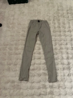 Ljusgrå tygbyxor från H&M, storlek S - . Bekväma, ljusgrå byxor i tyg med resår i midjan och dekorativa sömmar framtill. Byxorna har en smal passform. Längden på byxorna är nästan 102 cm . Väldigt fint skick