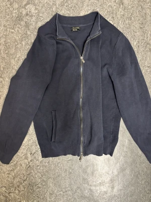 Mörkblå kofta från Massimo Dutti - Mörkblå kofta från Massimo Dutti i 100% bomull. Klassisk modell med hel dragkedja framtill, ribbade muddar och ståkrage. Perfekt till lager på lager och enkel att matcha med olika outfits.