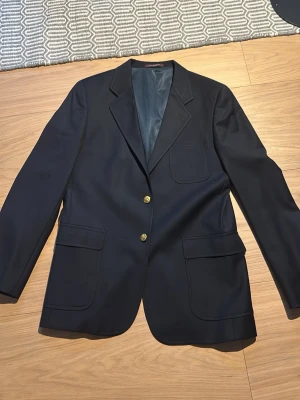 Svart kavaj med guldknappar - Snygg svart kavaj med två guldknappar framtill och tre utanpåliggande fickor. Klassisk passform och helfodrad insida. Perfekt för dig som vill ha en stilren och tidlös look.