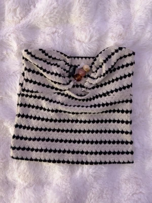 Randig bandeau tubtopp från H&M Divided - Säljer en bandeau tubtopp från H&M Divided i storlek XS. Toppen är randig i svart och beige med en mjuk, lite frottéliknande textur. Den är axelbandslös och har en enkel, rak passform som sitter snyggt på kroppen. 