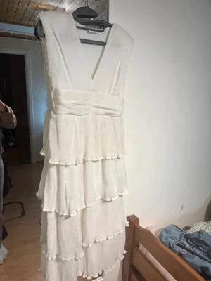 Vit långklänning med volanger - Säljer en studentklänning med flera lager volanger och v-ringning Har använt den en gång, som ny! Nypris: 1000 kr
