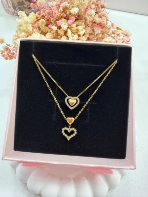 Två hjärtan – en perfekt kombination - Vackra hjärthalsband tillverkade i rostfritt stål och pläterade med 18K guld, dekorerade med gnistrande zirkonstenar som ger en feminin och elegant glans.  Smyckena är vattentåliga och allergivänliga, perfekta för daglig användning. Halsbanden är otroligt fina tillsammans i lager, men kan även köpas och bäras var för sig – helt efter din stil.  💰 Pris: • 175 kr styck • 300 kr för båda tillsammans  💛 En tidlös accessoar som passar både vardag och fest.