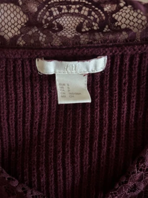 Vinröd stickad tröja med spets H&M - Mysig vinröd stickad tröja från H&M i storlek S. Tröjan har en v-ringning med dekorativ spetsdetalj runt halsen och ribbade muddar