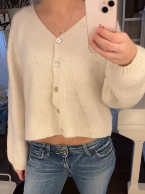 Vit kofta med knappar - Mysig ljusvit croppad kofta med v-ringning och knappar framtill. Tyvär finns det en liten fläck som har blivit av min kappa! (Bild 2) syns dock inte supermycket på 🤍
