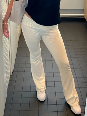 Vita bootcut byxor i mjukt material - Säljer ett par vita bootcut byxor med låg midja. Byxorna är gjorda i ett mjukt och stretchigt material som sitter skönt och följer kroppen. Perfekta för en avslappnad men ändå snygg look. Passar till sneakers eller sandaler.