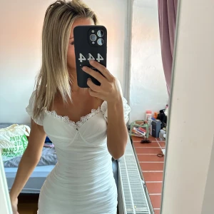 Vit kort klänning med spetsdetaljer - Supersöt vit kort klänning med puffärmar och smickrande tight passform. Klänningen har fina spetsdetaljer vid urringningen och lätt rynkade sömmar längs hela kroppen. Perfekt inför studenten!!!☺️☺️kommer m prislapp
