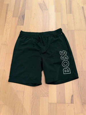 Hugo Boss shorts mörkgrön L - Stilrena HUGO BOSS shorts i mörkgrön färg med tydlig logga. Skönt material med resår och dragsko i midjan – perfekta för vardag, chill eller semester.  I mycket bra skick och sparsamt använda. 100 % original, etikett finns kvar.  📏 Storlek: L 🎨 Färg: Mörkgrön 📦 Skick: Mycket bra Kan skickas idag Pris kan diskuteras vid snabb affär 👌