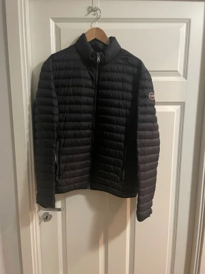 Svart pufferjacka från Colmar - Säljer en svart pufferjacka från Colmar med quiltad design och hög krage. Jackan har dragkedja framtill och två sidofickor med dragkedja. Insidan är ljusgrå och märket sitter på ärmen. Perfekt för dig som vill ha en stilren och varm jacka.