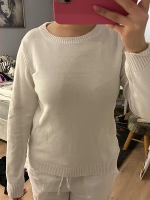 Vit stickad tröja med rund hals - En enkel och stilren vit stickad tröja med rund halsringning och ribbade muddar vid ärmslut och nederkant. Tröjan har lång ärm och en klassisk passform som funkar till det mesta. Perfekt för lager på lager under kyligare dagar.