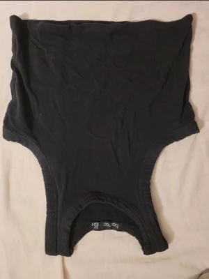 Svart tubtopp från Boohoo - En enkel svart tubtopp från Boohoo i mjukt bomullsmaterial. Toppen är axelbandslös och har en klassisk bandeauform som sitter tight mot kroppen. Perfekt att styla med jeans eller kjol för en clean look.