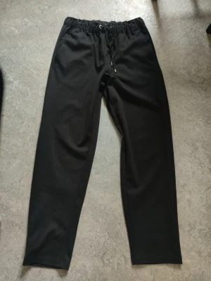 Svarta mjukisbyxor från 157, storlek S - Svarta mjukisbyxor från 157 med snörning i midjan och elastisk resår. Byxorna har en enkel och clean look, perfekta för chill dagar. Tillverkade i mjukt material som känns skönt mot huden.