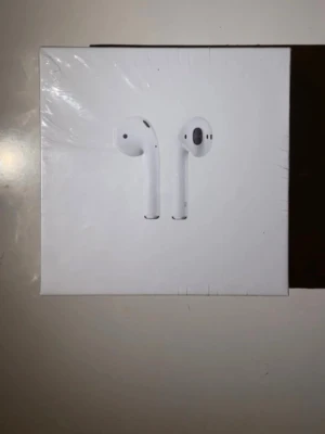 AirPods (2nd Generation) - Snygga och populära Apple AirPods med trådlöst laddningsetui. Komplett med originalförpackning, laddningskabel och manual. Perfekt för trådlös musik och samtal med hög kvalitet.