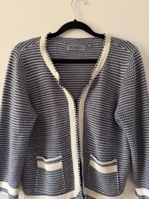 Randig kofta från Soaked in Luxury - Snygg randig kofta i mörkblått och vitt från Soaked in Luxury. Koftan har två fickor fram och vita kantdetaljer längs öppningen, ärmslut och nederkant. Den är stickad och har långärmad passform, perfekt för lager-på-lager under kyliga dagar. Första och sista knappen har gått av men den andra funkar och sitter fortfarande. Storlek M men passar XS/S också.