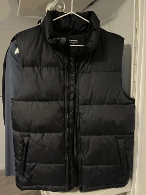Marinblå dunväst från Everest - Marinblå dunväst från Everest. Västen har två sidofickor och stängs med dragkedja framtill. Perfekt att slänga över en hoodie när det är kyligt ute. Materialet är syntet och dun, vilket gör den både lätt och varm. Använd fåtal gånger då den är för stor för mig, passar S/M.