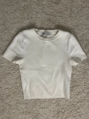 Vit topp från Zara - En stilren vit topp från Zara i storlek S. Modellen är croppad med korta ärmar och rund halsringning. Perfekt att matcha med jeans eller kjol för en clean look.