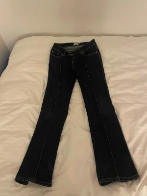 Bootcut mörkblå jeans från Lager 157 - Säljer ett par mörkblå bootcut jeans från Lager 157 med klassiska kontrastsömmar. Jeansen har låg midja och är tillverkade i slitstarkt denimmaterial.