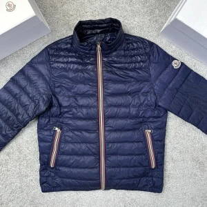 Mörkblå pufferjacka från Moncler - Säljer en mörkblå pufferjacka från Moncler med klassisk ståkrage och snygga ränder på dragkedjorna. Jackan har två sidofickor med dragkedja och Moncler-logga på ärmen. Perfekt för höst och vår och riktigt stilren. Jackan är i Storlek M och har små skador på ärmarna. 
