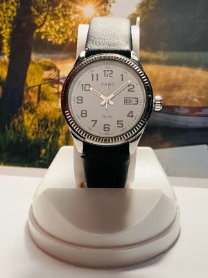 Casio Armbandsur - Klassisk Design  - Klassisk Casio armbandsur med en stilren design. Klockan har en vit urtavla med tydliga siffror och en datumvisning. Boetten är tillverkad i rostfritt stål och armbandet är i svart läder. Vattentålig 50M. Perfekt för både vardag och fest. Säljes i befintligt skick enligt bilderna, rustad med nytt batteri!