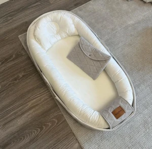 Bärbar babynest -  – 100% ekologisk bomull – Babynest kanter är fyllda med fiber – Tvättbar både in- & utvändigt, 30 grader – Medföljer en mindre skötväska samt babykudde. – Kan användas från födseln till ca 2 års ålder. – Produkten är Oeko-Tex Standard 100 certifierad vilket säkerställer att den är fri från skadliga kemikalier. Innermått: L:75cm x B:33cm x H:12cm Yttermått: L:93cm x B:48cm x H:12cm Fotdelen kan öppnas och förlängas upp till 93 cm 
