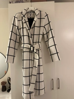 Vit rutig kappa med bälte  - Snygg vit kappa med svart rutigt mönster från bubbleroom