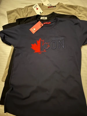 Mörkblå Dsquared2 ICON t-shirt - Snygg mörkblå t-shirt från Dsquared2 med broderad röd lönnlöv och texten ICON på bröstet. Klassisk rund hals och korta ärmar. Perfekt för dig som vill sticka ut med en ikonisk look. Materialet känns mjukt och skönt mot huden.