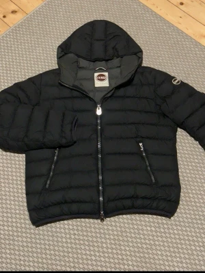 Colmar jacka - Säljer en svart pufferjacka från Colmar med huva och två sidofickor med dragkedja. Jackan har ett quiltat mönster och en stor Colmar-logga på ärmen. Perfekt för kalla dagar och har en schysst, sportig look. Skriv för fler frågor eller bilder, kan gå ner i pris vid snabb affär, storlek M/L