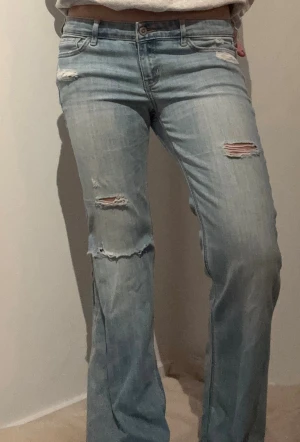Bootcut ljusblå jeans med slitningar - Säljer ett par ljusblå bootcut jeans med snygga slitningar och hål. Midjemått rakt över: 41 cm Innerbenslängd: 72 cm