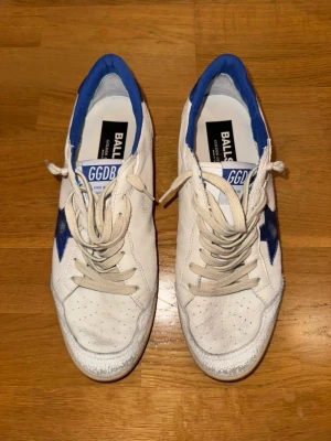 Golden Goose Ball Star vita sneakers med blå detaljer stl 41 - Golden Goose Ball Star sneakers i vitt skinn med blå stjärna på sidan och blå häl. Använda en gång. Säljer då dem är för stora, och jag inte kan lämna tillbaka då jag gjort mig av med skokartongen. Storlek 41 men sitter en aning större (passar 42-42.5). Köpta på Golden Goose’s hemsida, E-kvitto finns. Nypris 460€, säljer för 2199kr. Priset är en aning förhandlingsbart.