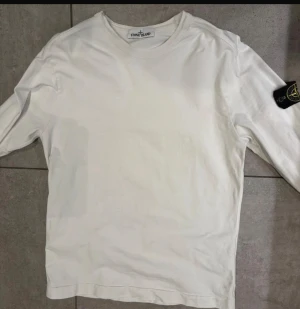 Vit långärmad t-shirt från Stone Island - Säljer en clean vit långärmad T-shirt från Stone Island med klassisk rund hals och ikonisk patch på vänster ärm. Tillverkad i mjuk bomull som känns skön mot huden. Perfekt för dig som gillar streetwear och vill ha en stilren look. Pris kan diskuteras 