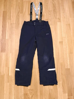 Polarn O. Pyret täckbyxor  - Mörkblå täckbyxor från Polarn O. Pyret med justerbara hängslen och reflexdetaljer på benen. Byxorna har elastisk midja och är fodrade för extra värme. Perfekta för vinterns alla äventyr utomhus. 