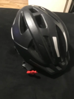 Svart cykelhjälm med LED-lampa - Säljer en svart cykelhjälm med vita detaljer och inbyggd LED-lampa baktill. Hjälmen har flera ventilationshål, justerbart spänne och vadderade remmar för extra komfort. Perfekt för dig som vill synas bättre i trafiken och samtidigt ha en snygg look.