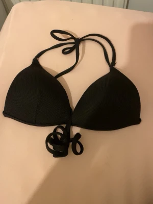 Svart push up bikiniöverdel med knyt S/XS - Säljer en stilren svart bikiniöverdel med knyt i nacken och ryggen. Insidan är vit och materialet känns mjukt och följsamt, perfekt för strandhäng. Enkel design utan mönster eller detaljer. Pris kan diskuteras