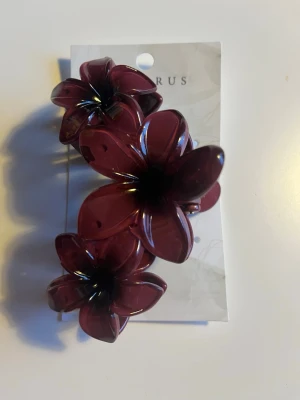 Vinröd hårklämma med blommor från Decorus - Snygg vinröd hårklämma från Decorus med stora blommor i plast. Perfekt för att ge frisyren en cool och unik touch. Klämman har en stabil fjäder och blommorna är tredimensionella och glansiga.