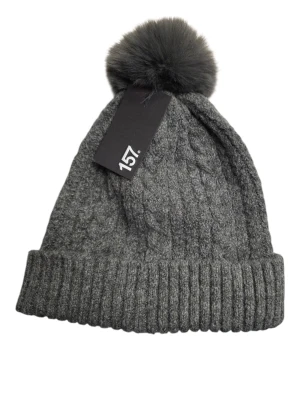 Mössa - Bilden visar en grå stickad mössa med en stor fluffig boll på toppen och ett märke från 157. Ingen väst syns på bilden.