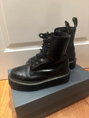 Svarta Dr. Martens boots med platåsula - Säljer ett par klassiska svarta Dr. Martens boots i läder med platåsula, snörning framtill och dragkedja på sidan. Modell Dr. Martens Jadon. I fint skick men inköpta 2019, tecken på användning. Man kan byta ut skosnören för att snygga till dem! Dragkedjan kärvar, se bild. Går fortfarande att använda