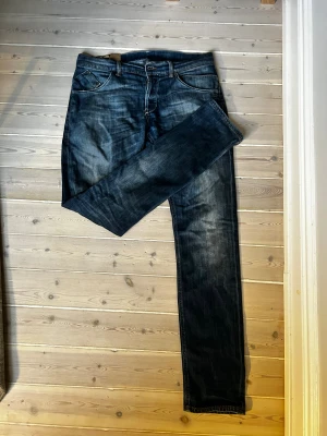 Blå jeans från Dondup - Snygga blå jeans från Dondup, tillverkade i Italien. Klassisk femficksmodell med raka ben och coola slitningar på låren och knäna. Jeansen har silverfärgade knappar med gravyr och kontrastsömmar. Perfekt för dig som gillar en tidlös och avslappnad look. Skick: 8/10. Nypris: ca 4000kr