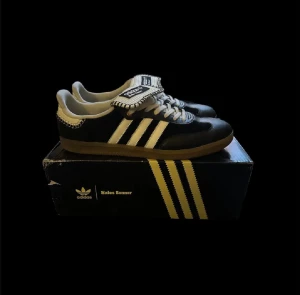 Adidas Samba Wales Bonner svart/vit - Adidas Samba Wales Bonner sneakers i svart och vitt med klassiska tre ränder på sidan. Skorna har en unik randig detalj på plösen och kontrasterande vita snören. Yttermaterialet är skinn och mocka, med en brun gummisula och rund tå. Perfekt för dig som gillar limited edition och snygg design. Pris kan diskuteras 