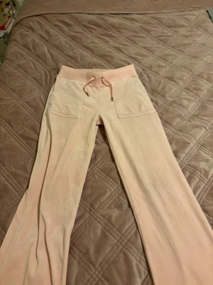 Ljusrosa mjukisbyxor Juicy Couture XS - Säljer ett par ljusrosa mjukisbyxor från Juicy Couture i storlek XS. Byxorna har bred resår i midjan med snörning, två framfickor och ett litet Juicy Couture-emblem på ena fickan. Materialet är mjukt och skönt, perfekt för chill dagar.