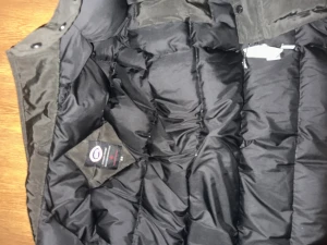 Äkta canada goose jacka utan luva - Svart dunjacka från Canada Goose med klassisk logga på ärmen. Jackan har flera fickor med knappar och dragkedja framtill. Perfekt för kalla dagar med sin tjocka och quiltade design. Snygg och funktionell för dig som vill ha både stil och värme.