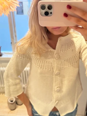 Vit stickad kofta med stora knappar - Säljer en vit stickad kofta med snygga stora knappar framtill och coolt mönstrad struktur vid krage och ärmslut. Koftan har trekvartsärm och en lite loose passform, perfekt att slänga över en t-shirt eller linne. Superfin till jeans eller kjol!