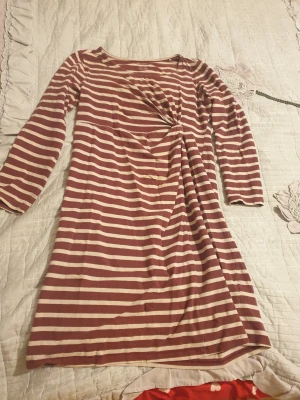 Randig klänning från Esmara L - Säljer en randig klänning från Esmara i storlek L. Klänningen har långa ärmar och är mönstrad med breda ränder i vinrött och beige. Den har en snygg twist-detalj framtill som ger en cool look. Materialet är mjukt och känns skönt mot huden.