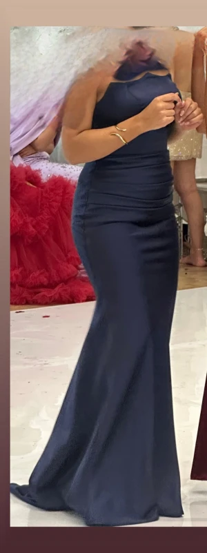 Marinblå långklänning med halterneck - Säljer en elegant marinblå långklänning med halterneck och figurnära passform. Klänningen har en slät yta och är sydd i ett mjukt, följsamt material som ger en snygg siluett. Perfekt för dig som vill ha en stilren look med lite extra edge. (HAR ANVÄNTS NÅGRA TIMMAR)