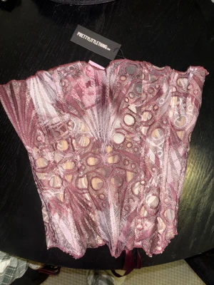 Mönstrad korsett från PrettyLittleThing - Säljer en snygg korsett från PrettyLittleThing med abstrakt mönster i vinröda toner. Toppen har snörning med satinband baktill. Aldrig använd, ny med prislapp på😍