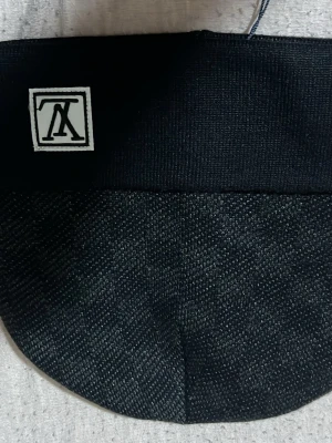 Svart väst från Louis Vuitton - Svart väst från Louis Vuitton med diskret struktur i tyget och klassisk logotyp på etiketten. Västen har en enkel, rundad form och bred kant nedtill. Materialet känns som en blandning av ull och syntet, vilket ger en lyxig och modern känsla.