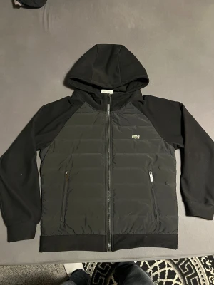 Svart lacoste jacka - Svart jacka från Lacoste med en skön och perfekt luva för dig som gillar att ha luvan på. Jackan har quiltad front och rygg, två sköna/stora fickor med dragkedja och klassisk Lacoste-logga på bröstet. Ärmar och luva är i mjukt tyg för extra komfort. Perfekt för denna vintern samt våren som inte är super kylig. Själv har jag använt den och den håller värmen perfekt 👌🏼 priset går o diskutera vid snabb affär så klart. Kan byta emot något fett