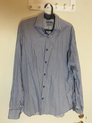Randig skjorta från Matinique - Snygg skjorta från Matinique med smala blå och vita ränder. Klassisk krage, långärmad och knappar framtill. Tillverkad i lättskött bomullsmaterial, perfekt för dig som vill ha en stilren look utan krångel.