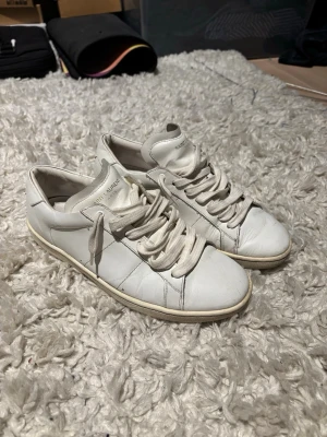 Vita Saint Laurent sneakers i skinn - Säljer ett par klassiska vita sneakers från Saint Laurent Paris. Skorna är i mjukt skinn med rund tå, platt sula och snörning. Diskret logga på plösen och hälen. Perfekta för en clean och stilren look. Storlek 39 men sitter 40