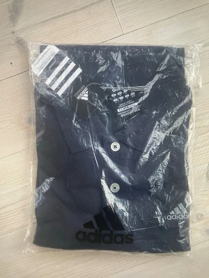 Mörkblå Adidas piké Clima365 - En golfpikétröja skapad för spel året om. Den ventilerande konstruktionen med Climacool ventilation absorberar fukt för att hålla dig torr under långa slag och nedförsbackar.  • Behaglig sval och torr känsla tack vare Climacool ventilation • Normal passform • Broderad logotyp på bröstet • Tre knappar i knappslå samt sprund i nederkant • Mjukt, stretchigt material för mycket bärkomfort och rörelsefrihet • Produktfärg: DarkNavy