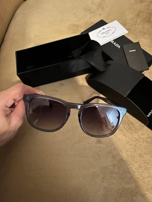Prada glasögon  - Bilderna visar ett par solglasögon från Prada med tillhörande fodral och förpackning. 
